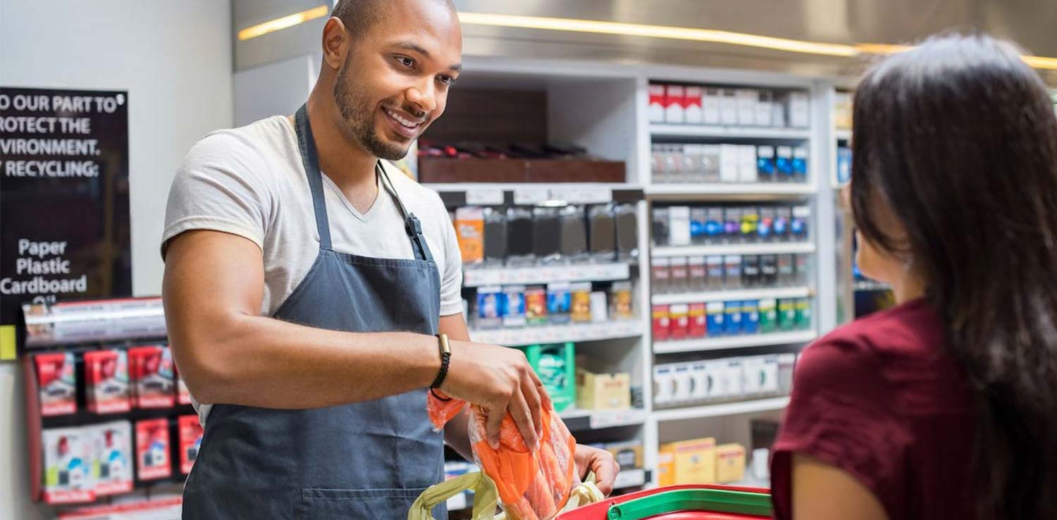 A smiling shop assistant serving a customer at a till in a retail store