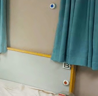 BellMe Call Button and B-A1-BC Cancel Button mounted by a bedside next to blue curtains