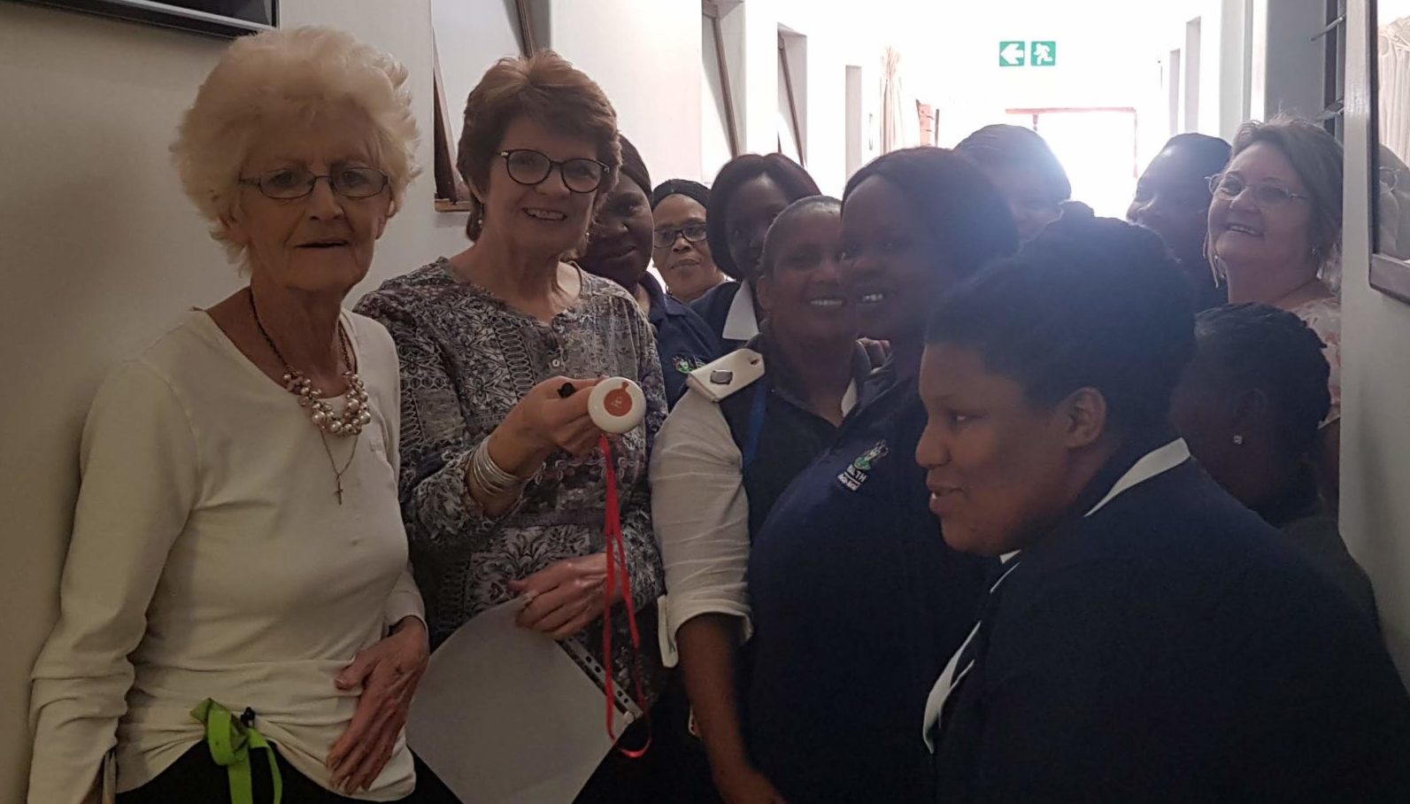 Residents and staff at a retirement facility holding up a BellMe emergency pendant in a corridor