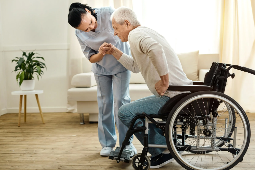 A nurse helping an elderly man from his wheelchair at home after he pressed his wireless call button